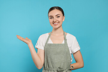 Wall Mural - Beautiful young woman in clean apron with pattern on light blue background