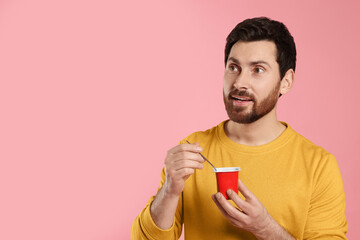 Handsome man with delicious yogurt and spoon on pink background. Space for text