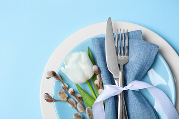 Festive table setting with willow twigs and tulip on light blue background, top view with space for text. Easter celebration