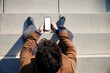 © baranq - Top view of man in coat sitting on stairs outside holding smartphone with blank white screen