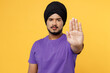 Strict serious devotee Sikh Indian man ties his traditional turban dastar wear purple t-shirt show stop gesture with palm isolated on plain yellow background studio portrait. People lifestyle concept.