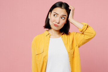 Wall Mural - Young pensive thoughtful mistaken sad woman of Asian ethnicity wears yellow shirt white t-shirt scratch hold head look aside isolated on plain pastel light pink background studio. Lifestyle concept.