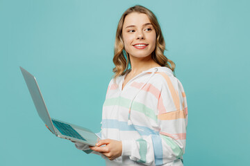 Side view young IT woman wears striped hoody hold use work on laptop pc computer chatting online looking aside isolated on plain pastel light blue cyan background studio portrait. Lifestyle concept.