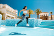 © shevtsovy - sporty woman running actively and jumping. Attractive fitness model jogging outdoors in sunny day. Swimming pool background.