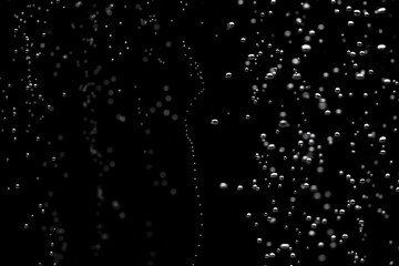 Shiny air bubbles underwater rising from bottom and illuminated by rays of light. Stream of oxygen bubbles on a black isolated background. Close up of a bubbling liquid during aeration of water.