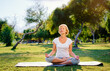 © luengo_ua - Yoga at park. Middle age woman in lotus pose sitting on green grass. Concept of calm and meditation.