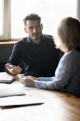 Wall Mural - Millennial business professional man talking to female coworker at office table, speaking, explaining work project details, tasks, plan, strategy. Corporate mentor training intern