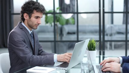 Wall Mural - Portrait of a smiling young businessman working on laptop and making notes on paper at office with his colleague.