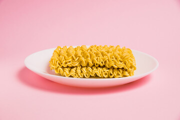 Instant noodles in a white plate on a pink background. Fast food in the modern world.