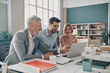© gstockstudio - Three happy business people looking at laptop while working in the office together