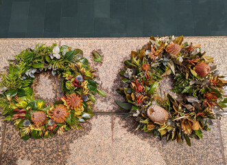 A closeup view of two wreaths placed on the edge of a pool of water, constructed using Australian native flowers .