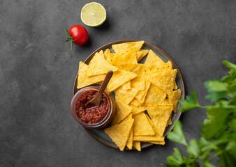 Wall Mural - Nachos or tortilla with spicy tomato sauce on a plate  with fresh herbs on a dark background. Corn chips with salsa sauce. Classic Mexican snack.