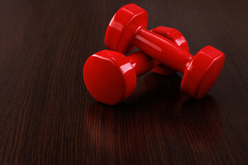 Two red shiny dumbbells lie on top of each other on a wooden floor. Selective focus.