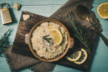 Wall Mural - Lemon rice risotto with rosemary and fresh lemon slices on light green background, top view