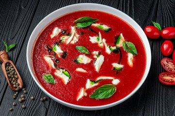 Wall Mural - Summer cold tomato vegetable soup Gazpacho with mozzarella cheese on the black table. Vegetarian cuisine.