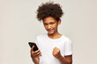 © Anatoliy Karlyuk - Portrait of angry frustrated male kid of african ethnicity in white t-shirt clenching fist trying to cope with anger while using low internet connection on his mobile phone, isolated on gray