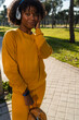 © Aydan - A girl in a yellow tracksuit listening to music in the park with headphones.