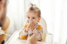 Portrait Of A Baby Girl Inhaling Medicine On Nebulizer By Her Own.