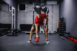 Cross fit training with kettle bell lifting. An attractive and muscular man in sportswear pumps his muscles and lifts a kettle bell in a modern gym. Strength, strong movement, arm and back workout