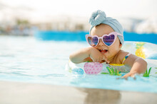 Cute Funny Toddler Girl In Colorful Swimsuit And Sunglasses Relaxing On Inflatable Toy Ring Floating In Pool Have Fun During Summer Vacation In Tropical Resort. Child Having Fun In Swimming Pool. 