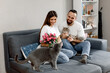 © VikaNorm - A couple in love is sitting with cats and pink tulips on the sofa at home.