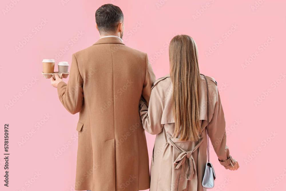 Young couple with cups of coffee on pink background, back view