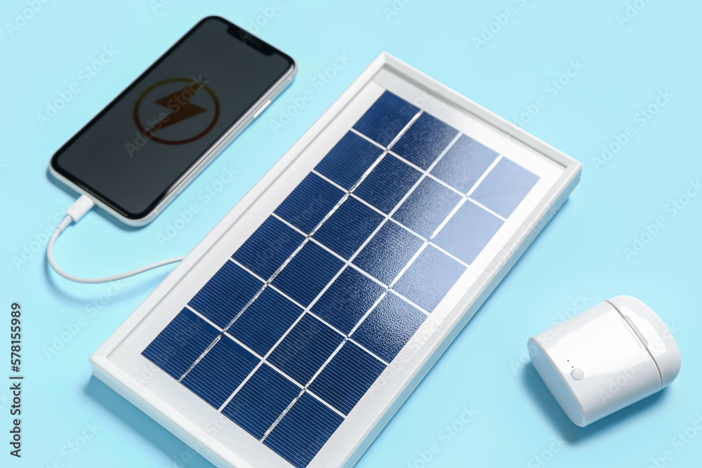Portable solar panel with mobile phone and earphones on blue background