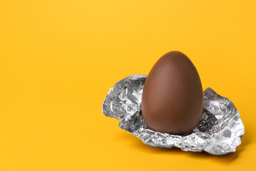 Wall Mural - Tasty chocolate egg with foil on orange background. Space for text