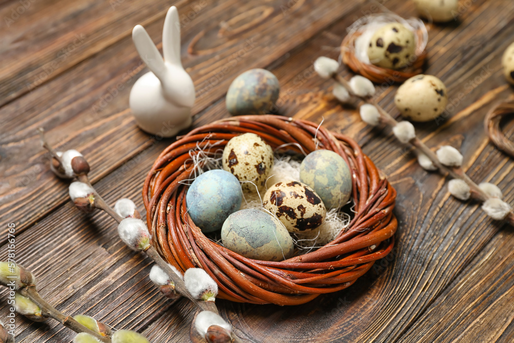 Easter quail eggs, pussy willow branches, bunny and wreath on wooden background