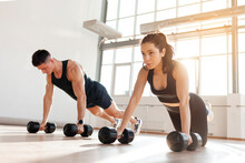 Athletic Couple In Sportswear In Training Do Push-ups With Dumbbells In The Fitness Room In The Morning