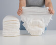 © Михаил Решетников - A woman chooses an adult diaper from a pile. Urinary incontinence problem.