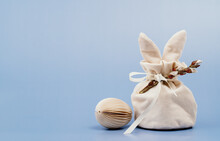 Easter Bunny Shaped Ivory Gift Bag With Sweets And Paper Craft Easter Egg On White Wooden Table, Blue Background Banner