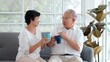 © M Stocker - Happy Asian senior old couple sitting on sofa in living room talking enjoying tea at home, smiling middle aged mature family chatting laughing drinking coffee having fun pleasant conversation together
