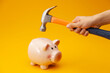 © Regisser.com - A pink piggy bank is about to be hit by a hammer. A hand holding a hammer which is raised above a pink china piggy bank, with a shocked and apprehensive facial expression. Financial problem.
