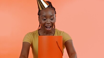 Poster - Black woman open birthday present, gift box and smile on wow face on studio background. Happy female model opening package for celebration, happiness or celebrate special excited event with party hat