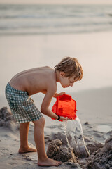 Wall Mural - Little boy in swimsuit playing with bucket near the sea, enjoying holiday.