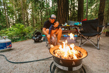 Dad And Son Roasting Marshmallows Over Propane Fire At Campsite