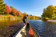 © Cavan Images - A man pulls a canoe through shallow water on a Maine river in fall.