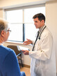 © Cavan Images - Doctor holding tablet speaking to older patient in a clinical setting.