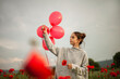 © Westend61 - Contemplative girl with poppy flower holding red balloons under sky