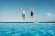 © Westend61 - Carefree couple with arms raised jumping in swimming pool