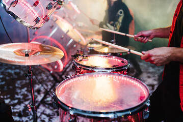 Man holding drum sticks, performing music. man plays musical percussion instrument on a black background. Drummer playing drum set at concert on stage. Music show. Bright scene lighting in club.