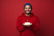 © Drobot Dean - Cheerful indian man holding birthday cake with candle isolated over red background