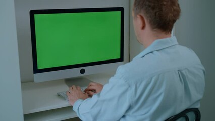 Poster - rear view man sitting at the workplace typing on white keyboard display with green screen freelancer working at home