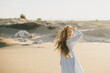 © polinaloves - Woman with long hair in a stylish dress poses in the desert sands.