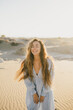 © polinaloves - Woman with long hair in a stylish dress poses in the desert sands.