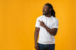 African man with beard pointing to copy space against yellow background