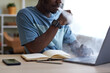 Close-up of African American male student smoking electronic cigarette in front of laptop while organizing work or preparing new project