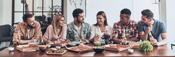 Canvas Print - Group of cheerful young people having dinner with pizza indoors together