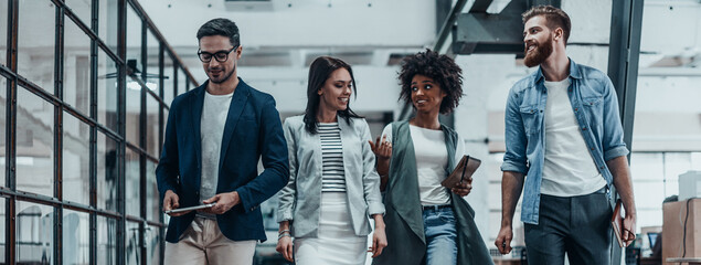 Poster - Group of happy young people discussing business while walking through the office corridor